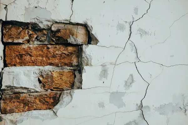 Çürüme ve yaşlanma belirtileri gösteren çatlak boyalı eski bir tuğla duvarın detaylı görüntüsü. Yıpranmış tuğla bir duvara yakın çekim yapmak, yapı malzemesinin eskimiş dokusunu ortaya çıkarır..