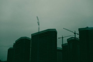 Şehrin bulutlu gökyüzüne karşı modern gökdelenler inşa ediliyor. Gökyüzüne uzanan vinçlerle modern yüksek binalar yapım aşamasında. 
