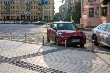 Kyiv, Ukrayna 7 Haziran 2025 Red Suzuki Swift güneşli bir günde Avrupa 'da bir kaldırım taşı sokağına park etti. Diğer araba ve binaların görüldüğü yerde canlı bir araba. Metalik park balonları.
