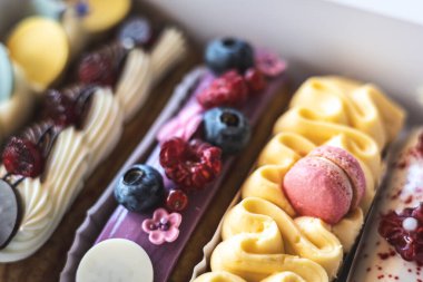 Taze böğürtlen ve kurabiye dolu nefis ekekler bir fırın kutusunda güzelce sergileniyor. Taze böğürtlen ve dekoratif kremayla süslenmiş renkli eklerdendir. Kremalı tatlılar ve ikramlar. 