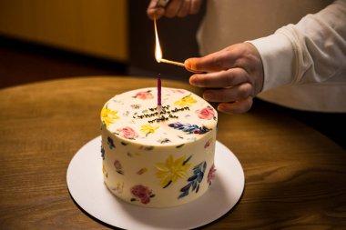 Bir el pastanın üzerine mum yakıyor. Çiçeklerle süslenmiş, eğlenmeye hazır. Bir el, güzel bir doğum günü pastasının üzerine mum yakar. Bir şenlikli pasta çiçeklerle süslenir.. 