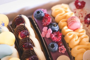 Taze böğürtlen ve kurabiye dolu nefis ekekler bir fırın kutusunda güzelce sergileniyor. Taze böğürtlen ve dekoratif kremayla süslenmiş renkli eklerdendir. Kremalı tatlılar ve ikramlar. 