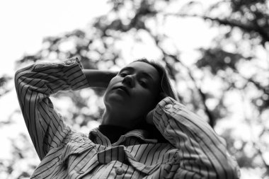 Çizgili tişörtlü düşünceli bir kadın, elleri başının arkasında tek renkli siyah beyaz bir kız kameraya bakıyor. İnsanlar doğada dinleniyor. Farkındalık, yalnızlık zihinsel sağlık konsepti