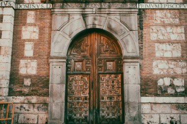 Alcala de Henares, Madrid 1 Ekim 2024 Eski tuğla bir binanın girişinin odak noktası mükemmel oyulmuş ahşap bir kapıdır. Kemerli ahşap bir kapının ayrıntılı bir görüntüsü..
