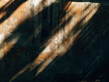 Soyut desenli duvar, güneşten gelen gölgelerle görsel bir zıtlık yaratıyor. Dokulu duvar, güneşten sırılsıklam olmuş, bir ışık ve gölge oyunu yaratıyor, mimari detayları vurguluyor..