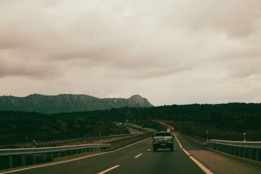 Madrid, İspanya 1 Ekim 2024 Bir kamyonet açık bir otoyolda dağlara doğru gidiyor. Bir kamyonet bulutlu bir gökyüzünün altındaki uzak dağlara doğru otoyolda ilerliyor. Yol gezisi..