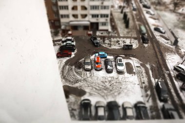 Dairelerin yakınındaki karla kaplı bir otoparkta arabaların park edildiği bir kış sahnesi. Bir apartmanın önündeki karla kaplı arsanın yüksek açılı görüntüsü, park halindeki arabaların kış atmosferine dokunuşu..