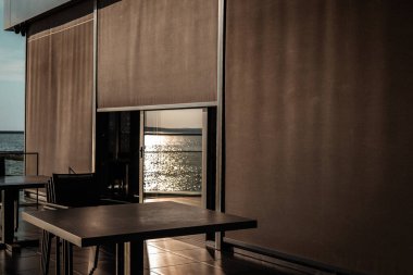 Modern bir restoran terasında deniz manzaralı sakin bir yemek deneyimi sunulur. Okyanus manzaralı, masaları, sandalyeleri ve cam parmaklıkları olan zarif bir açık hava yemek alanı. Tatil köyü..