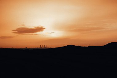 Güzel gün batımı gökyüzünü canlı turuncuya boyar ve manzaranın üzerine sıcak bir parıltı saçar. Turuncu renkler ve siluetli toprak ve ufuk üzerinde sıcak bir parıltıyla nefes kesen bir gündoğumu silueti..