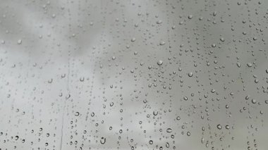 Islak pencereye düşen yağmur damlalarının yavaş çekim makrosu. Su damlacıklarına yakın çekim. Açık hava manzarası camdan görülebiliyor. Damlacıklar güzel bir doku efekti yaratıyor Sonbahar havası