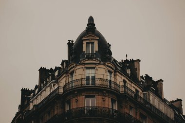 Paris, Fransa 2 Ekim 2024 Parisli bir binanın mimari detayları bulutlu bir gökyüzüne karşı. Süslü balkonları ve kubbeli çatısı olan, sessiz, bulutlu bir gökyüzüne karşı kurulmuş klasik bir binanın köşesi.