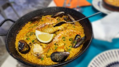 Klasik İspanya yemeği, beyaz ahşap arka plan manzaralı geleneksel tavada deniz ürünleri paella. İspanyol paellası, karides, kıskaç, midye, yeşil bezelye, taze limon dilimleri, mesaj için boşluk.