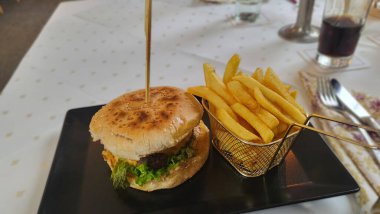 Sulu bir cheeseburger susamlı ekmeğin üzerinde yanında kızarmış altın patates ile servis edilir..