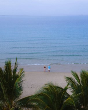 Gün batımında kumsalda yürüyen bir çift kadın ve erkek Koh Chang 'deki Klong Prao Sahili' nde İHA görüntüsü turkuaz renkli okyanusun yukarısından drone görüntüsü.. 