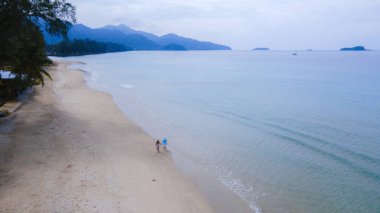 Gün batımında kumsalda yürüyen bir çift kadın ve erkek Koh Chang 'deki Klong Prao Sahili' nde İHA görüntüsü turkuaz renkli okyanusun yukarısından drone görüntüsü.. 
