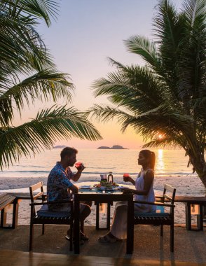 Koh Chang adasında, Tayland 'da tropikal bir plajda gün batımında romantik bir akşam yemeği. Erkekler ve kadınlar gün batımında balayı yemeği