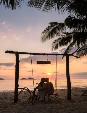 Birkaç erkek ve kadın salıncakta Koh Chang Tayland adasındaki tropik bir plajda gün batımını izliyorlar.. 