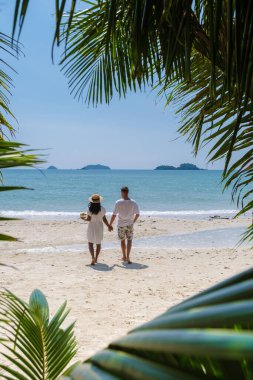 Tayland 'da sahilde yürüyen bir çiftin palmiye yaprakları arasındaki manzara. Erkekler ve kadınlar Koh Chang 'de tropik bir plajda yürüyorlar.