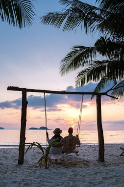 Gün batımında Koh Chang Tayland sahilinde salıncakta sallanan çift. Tayland 'da tatilde olan erkekler ve kadınlar.