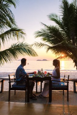 Koh Chang Tayland sahilinde romantik bir akşam yemeği yiyen çift. Erkekler ve kadınlar sahilde akşam yemeği boyunca gün batımını izliyorlar.