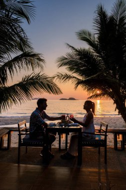 Koh Chang Tayland sahilinde romantik bir akşam yemeği yiyen çift. Erkekler ve kadınlar sahilde akşam yemeği boyunca gün batımını izliyorlar.