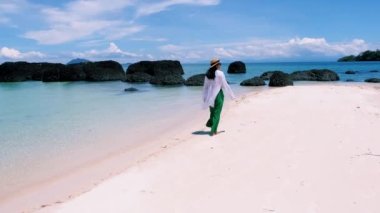 Koh Mak yakınlarındaki Koh Kham Tayland adasında tropikal bir plajda yürüyen Asyalı kadınlar.