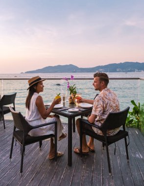 Phuket Tayland adasında gün batımında Tayland yemeğiyle sahilde romantik bir akşam yemeği. Birkaç erkek ve kadın sahilde romantik bir akşam yemeği yiyor.