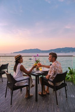 Phuket Tayland adasında gün batımında Tayland yemeğiyle sahilde romantik bir akşam yemeği. Birkaç erkek ve kadın sahilde romantik bir akşam yemeği yiyor.