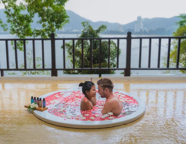 couple in bath tub with rose petals. men and women in a bath tub looking out over the ocean