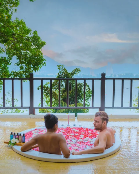 couple in bath tub with rose petals. men and women in a bath tub looking out over the ocean