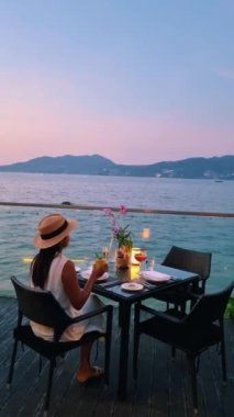 Phuket Tayland adasında gün batımında Tayland yemeğiyle sahilde romantik bir akşam yemeği. Kadınlar sahilde romantik bir akşam yemeği yiyorlar.