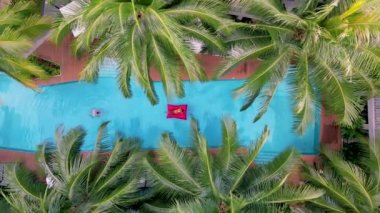 Yüzme havuzunda palmiye ağaçları olan bir çift yüzme havuzunun yukarısından görünüyor, bir kaç erkek ve kadın yüzme havuzunda, drone manzaralı.. 