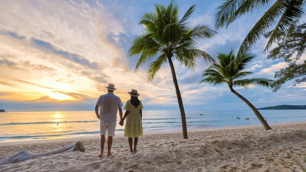 两名男男女女站在一棵棕榈树旁 用白色的沙子和棕榈树看着沙滩上的落日 — 图库照片