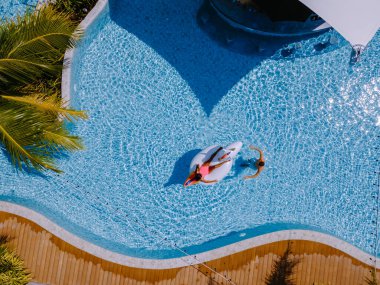Palmiye ağaçlarıyla dolu havuzda drone görüntüsü, birkaç erkek ve kadın yüzme havuzu manzaralı, tropik bir bahçeden, palmiye ağaçları olan.