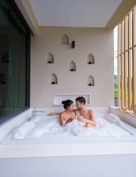 在度蜜月期间 一对夫妇在按摩浴缸里喝着香槟 亚洲的泰国女人和坐在浴缸里的高加索男人在按摩浴缸里 — 图库照片