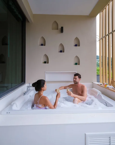 在度蜜月期间 一对夫妇在按摩浴缸里喝香槟 亚洲的泰国女人和坐在浴缸里的高加索男人在阳台上 — 图库照片