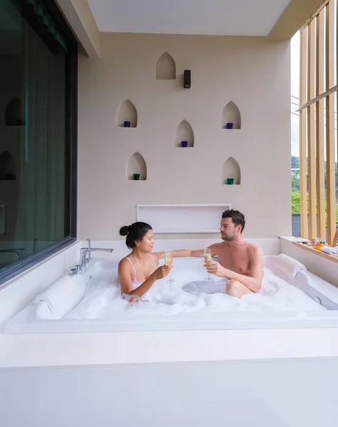 couple drinking champagne in a jacuzzi during honeymoon vacation, Asian Thai women and caucasian men in a outside bathtub jacuzzi