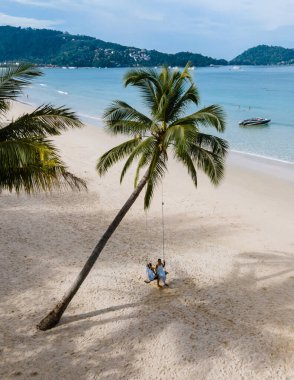 Birkaç erkek ve kadın Patong Phuket Tayland sahilinde palmiye ağacının altında salıncakta sallanıyor.. 