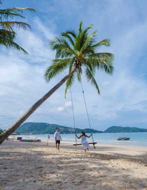 Birkaç erkek ve kadın, güneşli bir günde, Patong Phuket Tayland sahilinde palmiye ağacının altında salıncakta sallanıyorlar. 