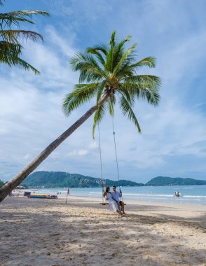 Birkaç erkek ve kadın, güneşli bir günde, Patong Phuket Tayland sahilinde palmiye ağacının altında salıncakta sallanıyorlar. 