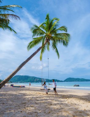 Birkaç erkek ve kadın, güneşli bir günde, Patong Phuket Tayland sahilinde palmiye ağacının altında salıncakta sallanıyorlar. 