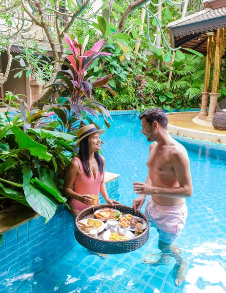 A couple having breakfast in the pool during vacation, men, and women in the pool with floating breakfast.