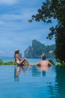 Birkaç beyaz erkek ve Taylandlı kadın sonsuz havuzda Koh Phi Tayland sahiline bakıyorlar.