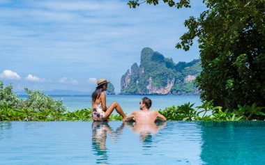 Sonsuzluk havuzunda bir çift kadın ve erkek Koh Phi Tayland sahiline bakıyorlar.