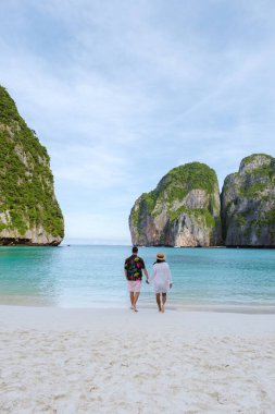 Taylandlı kadınlar ve beyaz erkekler sabahları turkuaz renkli okyanuslarla Maya Körfezi sahilinde Koh Phi Phi Tayland 'da yürürler.. 