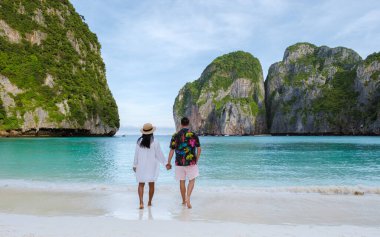 Taylandlı kadınlar ve beyaz erkekler sabahları turkuaz renkli okyanuslarla Maya Körfezi sahilinde Koh Phi Phi Tayland 'da yürürler.. 