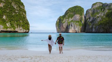 Taylandlı kadınlar ve beyaz erkekler Maya Körfezi plajında yürüyorlar Koh Phi Phi Tayland 'da turkuaz renkli okyanuslarla. 