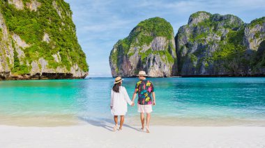Taylandlı kadınlar ve şapkalı beyaz adamlar Maya Körfezi sahilinde yürüyorlar Koh Phi Tayland