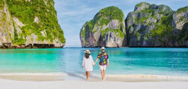 Taylandlı kadınlar ve şapkalı beyaz adamlar Maya Körfezi sahilinde yürüyorlar Koh Phi Tayland