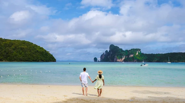 朝の太陽の下でターコイズブルーの海と共にビーチを歩く男女のカップルであるコ — ストック写真